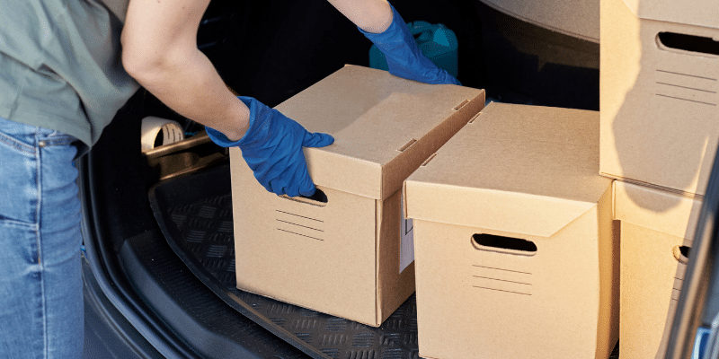 A person pulling banker boxes full of documents out of their car trunk